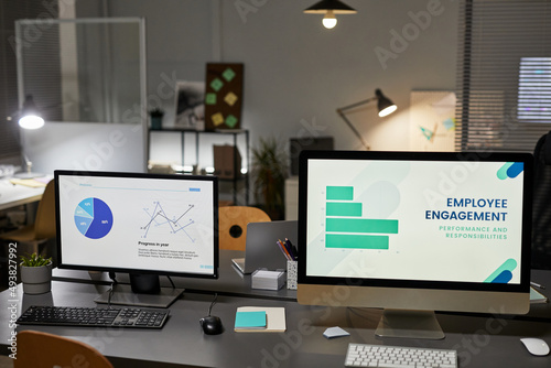 Background image of two computer monitors in office with Employee engagement charts, copy space