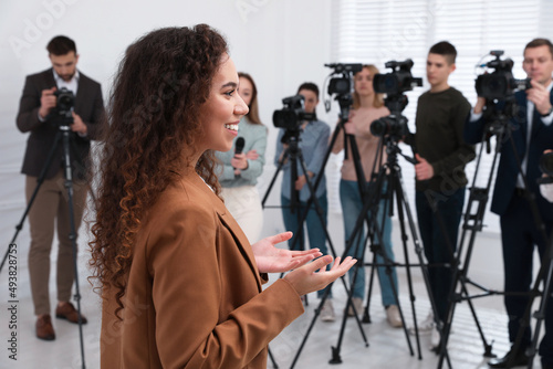 Canvas Print Happy African American business woman talking to group of journalists indoors