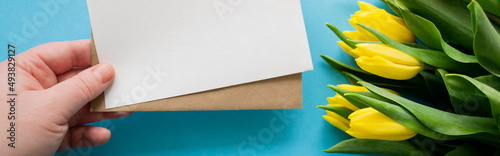 Banner with hand holds envelope and paper for text on blue background and yellow tulips. Happy holiday greetings