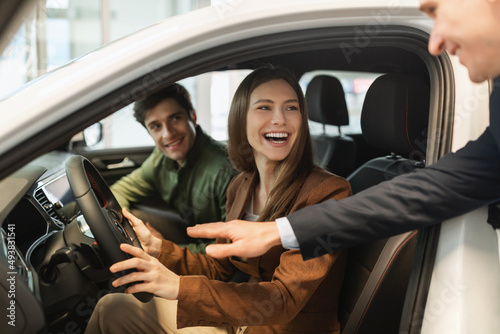 Happy young couple test driving new car, salesman helping them make best choice at auto dealership © Prostock-studio