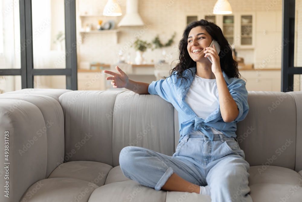Happy millennial brunette woman sitting on sofa, making call on mobile phone at home, free space Happy millennial brunette woman sitting on sofa, making call on mobile phone at home, free space