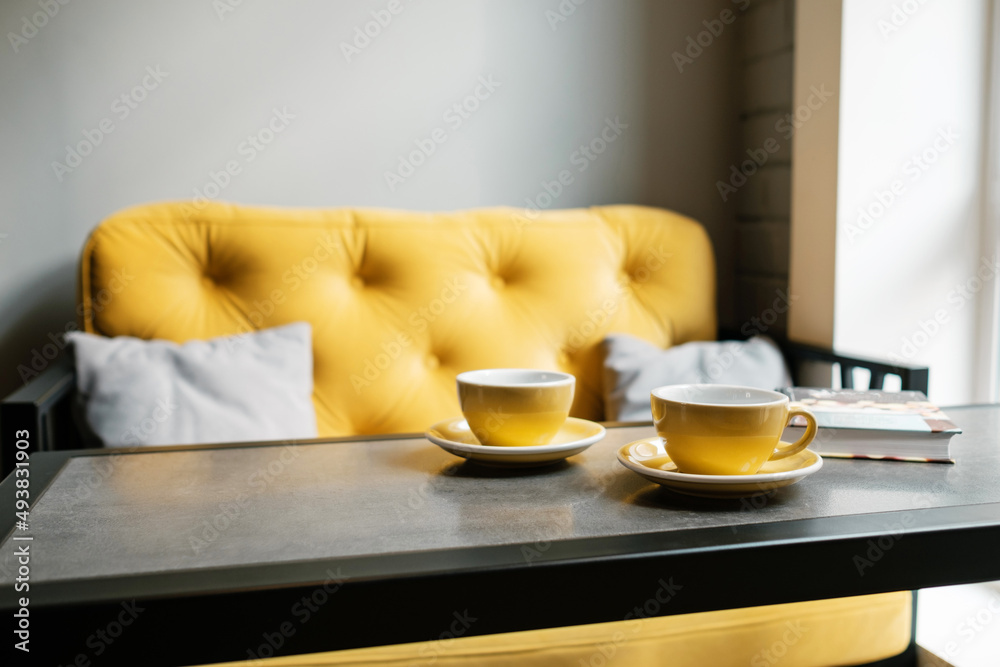 A couple of cups of coffee in an empty cafe. Yellow dishes and a sofa in a restaurant. No guests.