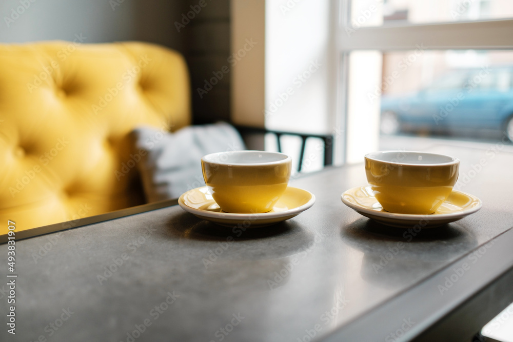 A couple of cups of coffee in an empty cafe. Yellow dishes and a sofa in a restaurant.