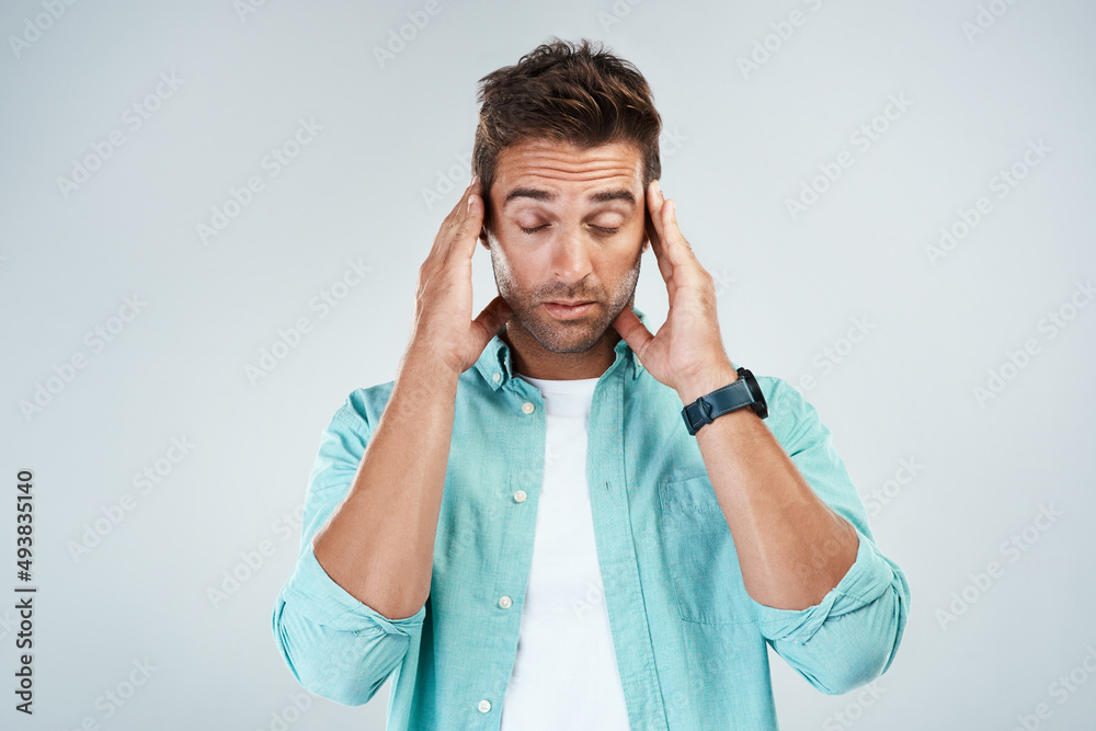 I cant concentrate properly. Studio shot of a young man with an uncomfortable facial expression due to a headache while standing against a grey background. I cant concentrate properly. Studio shot of a young man with an uncomfortable facial expression due to a headache while standing against a grey background.