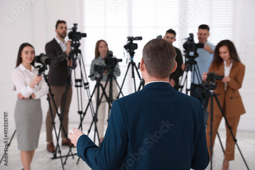 Canvas Print Business man talking to group of journalists indoors, back view