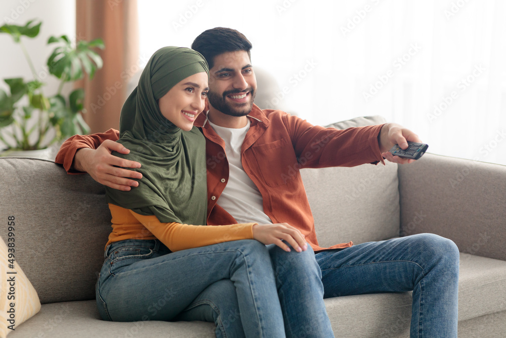 Side View Of Happy Middle Eastern Spouses Watching TV Indoors Side View Of Happy Middle Eastern Spouses Watching TV Indoors