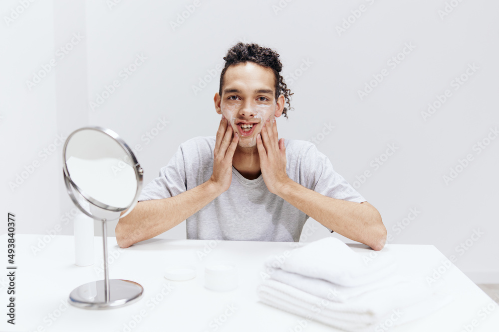 portrait of a man puts cream on the face but sitting at the table in front of the mirror light background portrait of a man puts cream on the face but sitting at the table in front of the mirror light background