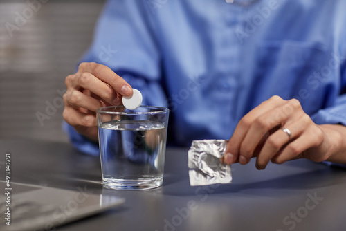 Close up of unrecognizable businesswoman putting fizzing pill into glass of water at workplace, copy space