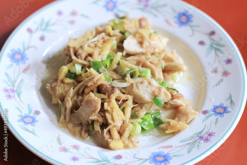 Ginger-fried chicken with sliced spring onions served on a white floral plate on an orange dining table.