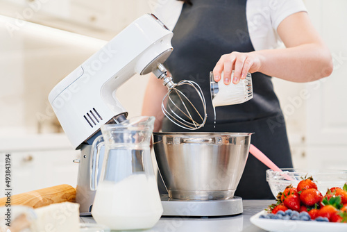 Photos A women cook adds a milk to prepare dough or cream in a mixer bowl
