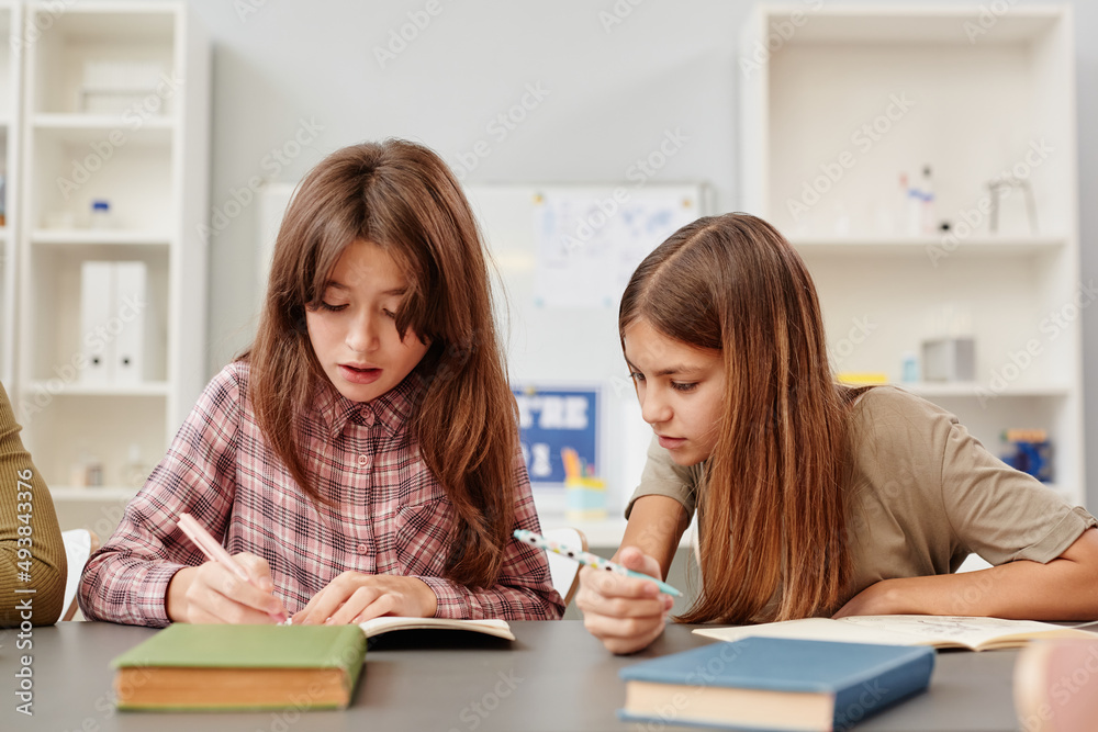 Portrait of young girl looking into friends notebook while copying test answers in school Portrait of young girl looking into friends notebook while copying test answers in school