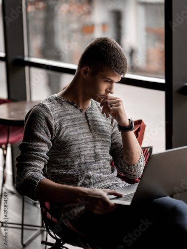 handsome man sitting in a cafe by the window with a laptop