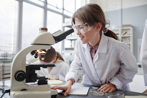 Papier peint Side view portrait of smiling young girl looking into microscope while enjoying