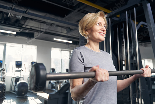 Cheerful woman doing exercise with barbell in gym