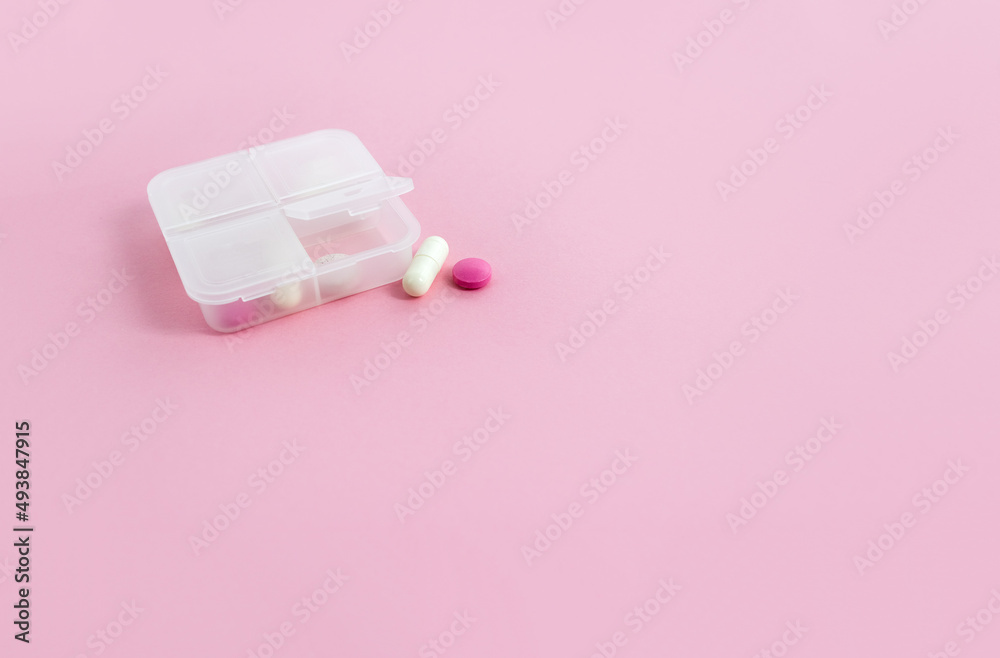 Pill box and tablets on pink background. Minimal concept of taking medications. Copy space, selective focus Pill box and tablets on pink background. Minimal concept of taking medications. Copy space, selective focus
