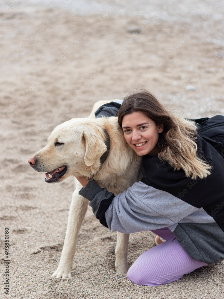 Young woman hugs dog at beach. She is so happy. Big smile. Vertical photo. Friendship, animal love. Young woman hugs dog at beach. She is so happy. Big smile. Vertical photo. Friendship, animal love.