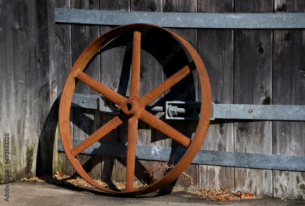 Iron Wheel Stands Rusting Against Wooden Building