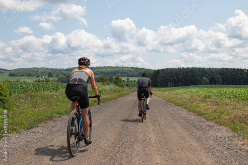 Vue de dos d'un couple de cyclistes faisant du vélo de gravelle sur une route tranquille dans la campagne par une journée d'été, ensoleillée.