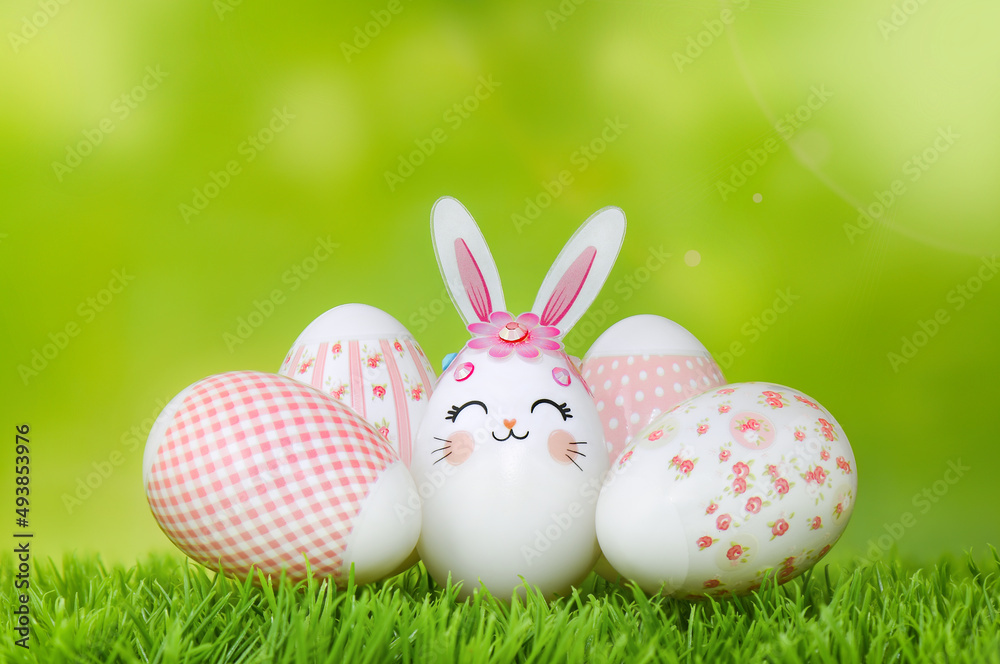 Easter eggs on the grass. Bunny egg and pink-decorated eggs against spring green bokeh background. Happy Easter composition.