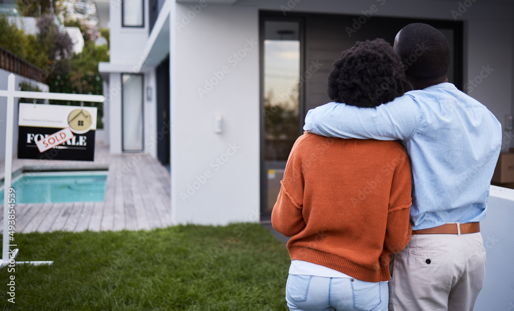 This dream home is finally ours. Rearview shot of a young couple standing outside their new home.