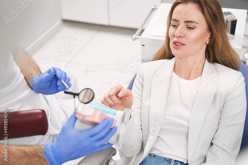 Woman discussing tooth model with dentist in dental clinic