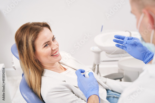 Dentist showing dental floss to woman in dental clinic