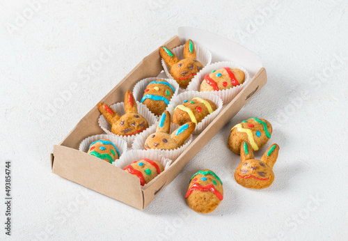 Little Easter cookies in the shape of eggs and rabbits, decorated with colorful icing sugar, in a serving box. Light background
