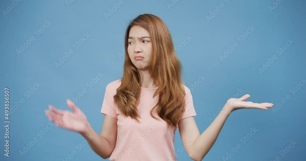 Youth Asia lady wear casual pink bad mood throwing up hands with uncertainty on face unhappy upset stand isolate over blue background, I don't like it, People emotions lifestyle, Copy space concept. Youth Asia lady wear casual pink bad mood throwing up hands with uncertainty on face unhappy upset stand isolate over blue background, I don't like it, People emotions lifestyle, Copy space concept.
