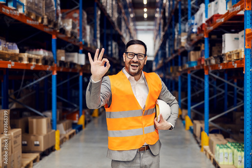 A businessman in warehouse showing okay gesture and smiling at the camera.