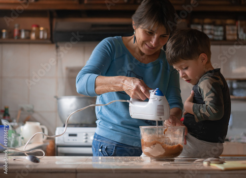 Latin mature grandmother and preschool grandson bonding while making a chocolate cake at home. Family love, joy and food heritage concept.