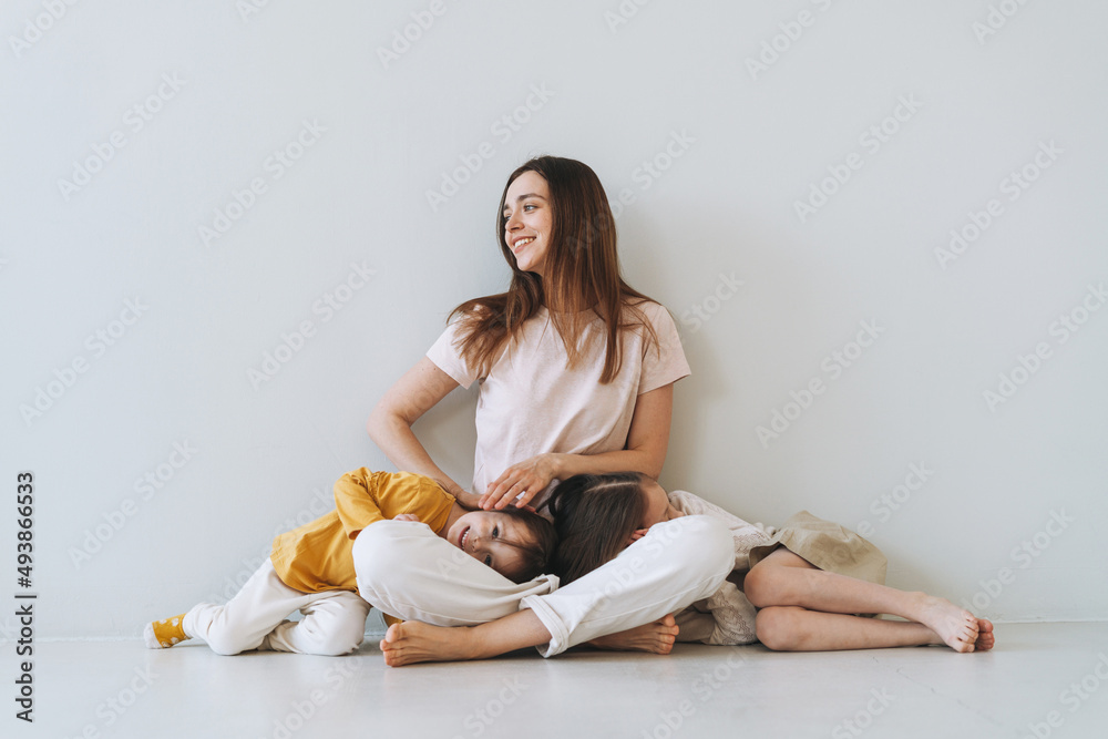 Young happy mother with two children girls on the background of gray wall Young happy mother with two children girls on the background of gray wall