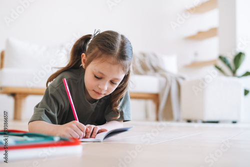 Preschool little girl is lying on the floor and drawing at bright room at the home