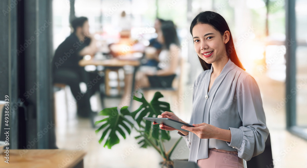 Elegant asian businesswoman standing in office with digital tablet, smiling and looking at camera.