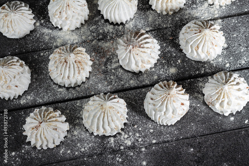 Sweet meringue, delicious and light dessert. Culinary background with vanilla meringue on dark wooden background, sprinkled with nuts, cocoa and powdered sugar. Still life in style of food.