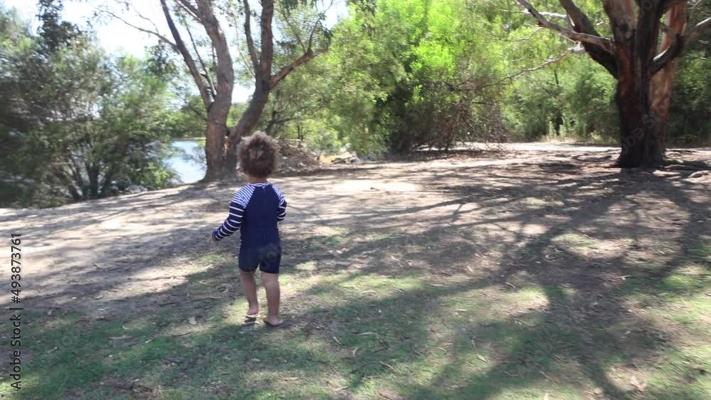 A young little mixed raced boy runs in slow motion in the bush along the shores of a lake. A young little mixed raced boy runs in slow motion in the bush along the shores of a lake.