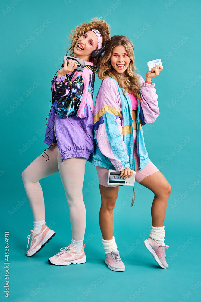 Were out spreading some 80s vibes. Studio shot of two beautiful young women  styled in 80s clothing. Stock Photo