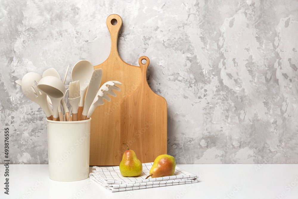 Cooking utensil set on kitchen table. Silicone kitchen tools, wooden cutting boards, mortar bowl with pestle. Front view Copy space Cooking utensil set on kitchen table. Silicone kitchen tools, wooden cutting boards, mortar bowl with pestle. Front view Copy space
