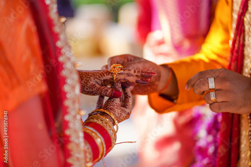 Tender hands of an Indian bride covered with henna tattoo hold groom's hand while he gives her a wedding ring.