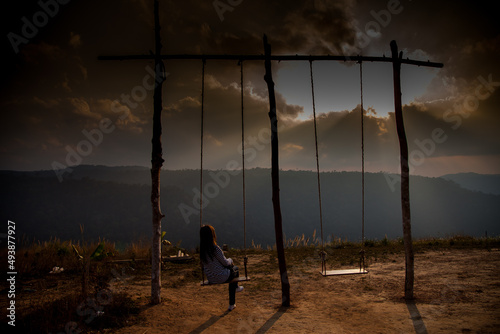 Lonely woman watching sunset alone sitting on swings on the mountain at sunset.