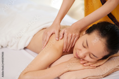 Hands of masseur massaging back of young female client with oils on massage table