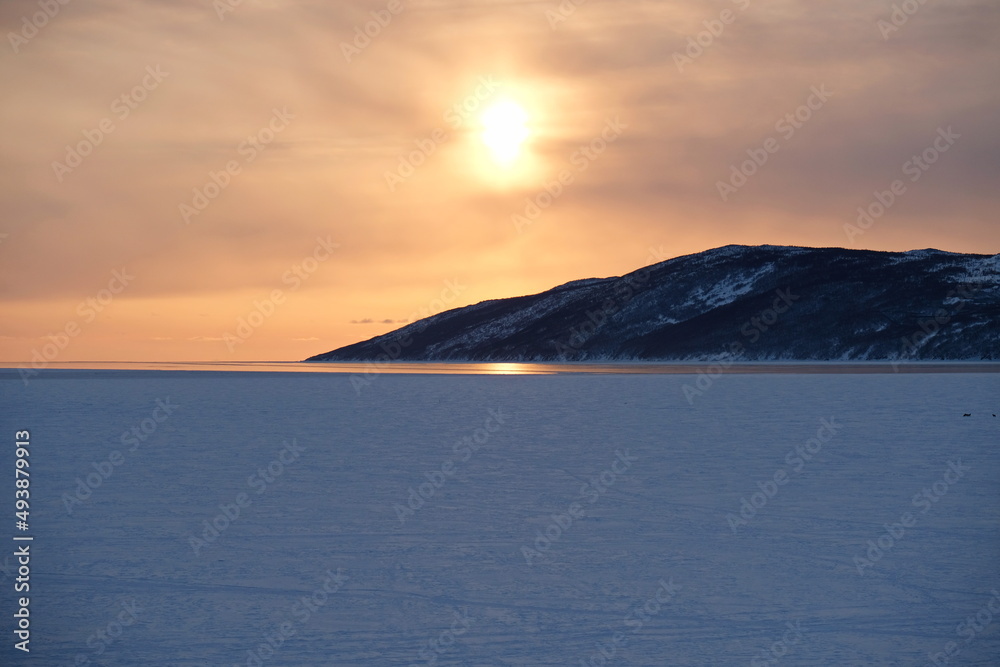 The setting sun over the icy river and the stone slope.