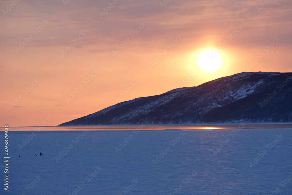 The setting sun over the icy river and the stone slope.