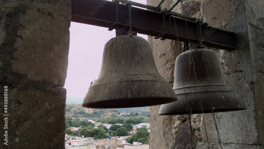 Church bells mounted in high tower in the public square of a small mexican town, that can be heard by the surrounding community. Church bells mounted in high tower in the public square of a small mexican town, that can be heard by the surrounding community.