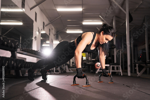 side view of a beautiful athletic girl, dressed in a black sports top and tights, does push-ups during an intensive workout in the gym. Healthy lifestyle, gymnastics concept,
