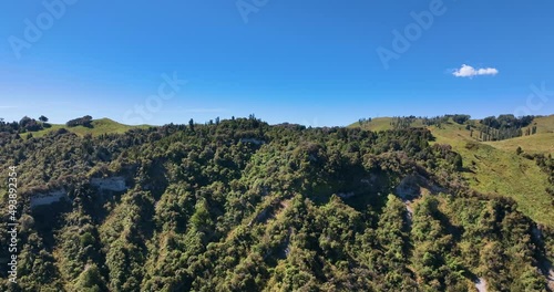 Flight towards, and close-up, of bush covered New Zealand farming hilltop photo