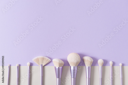 Makeup brushes set in row. Professional makeup tools on violet background. Set of glamour make up brushes. Magazines, social media. Visagist tools. Copy space. Creative flat lay. Cosmetics and beauty.