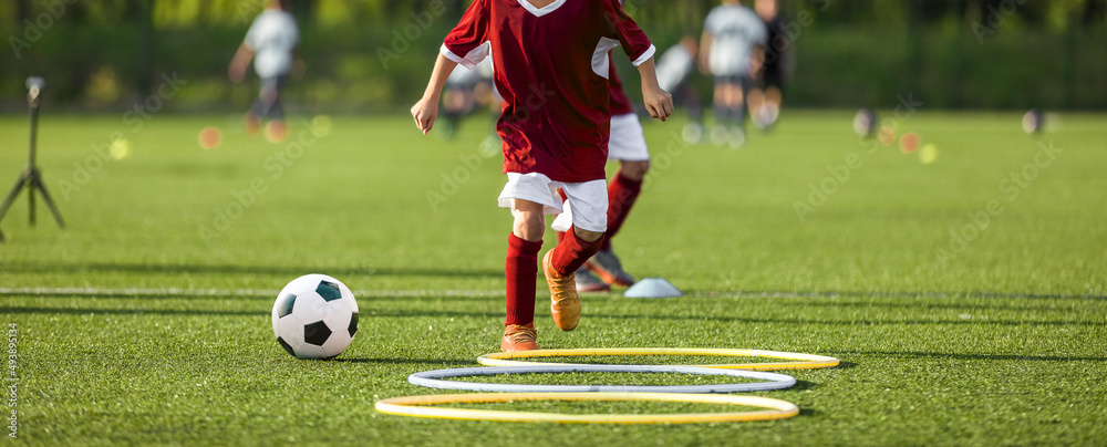 Children on agility sports soccer training. Young boy jumping over hula hoops on hurdles trail Children on agility sports soccer training. Young boy jumping over hula hoops on hurdles trail