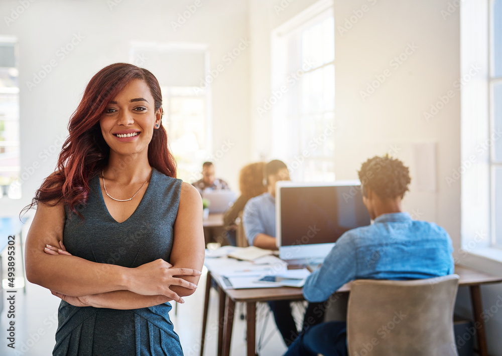 Running her office with confidence and determination. Portrait of a confident young woman working a modern office with her team in the background. Running her office with confidence and determination. Portrait of a confident young woman working a modern office with her team in the background.