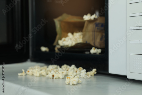 Open microwave oven with fresh popcorn on table, closeup