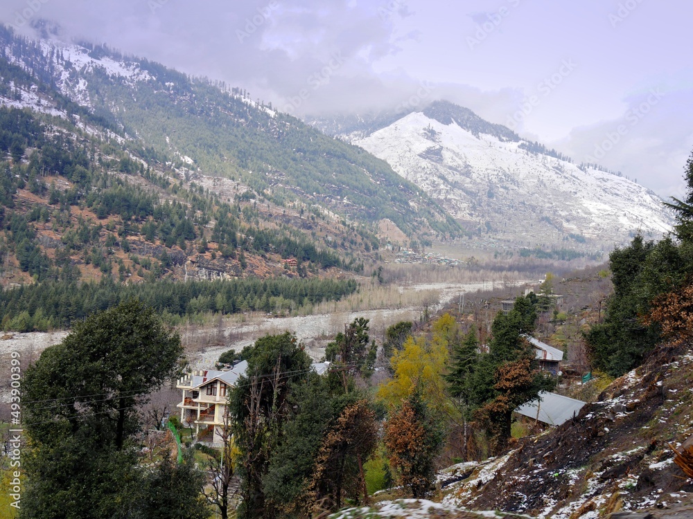 Medium wide shot of Himalayas landscape along Beas River with snow-capped mountains in the distance